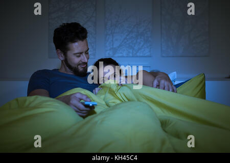 Couple lying in bed and watching scary movies on tv, the man is holding a remote control Stock Photo