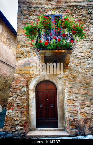 Entrance Door of a Mediavel House and a Small Balcony with Flowers, Pienza, Tuscany, Italy Stock Photo