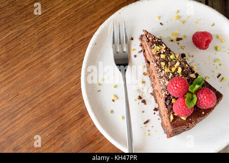 Slice of chocolate cake topped with raspberries, pistachio nut and mint leaf on white plate. Copy space for text. Top view Stock Photo