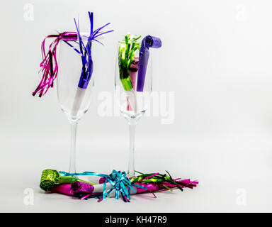 The morning after-2 champagne flutes filled with colorful New Years Eve noisemakers isolated on a solid background Stock Photo