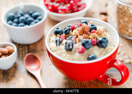 Oatmeal porridge bowl with blueberries, nuts and raspberries. Jar of granola on side. Healthy colorful breakfast for kids. Closeup view, selective foc Stock Photo