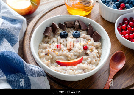 Colorful and healthy breakfast for kids: oatmeal porridge with berries, nuts and organic chocolate with a funny face. Meal for kids Stock Photo