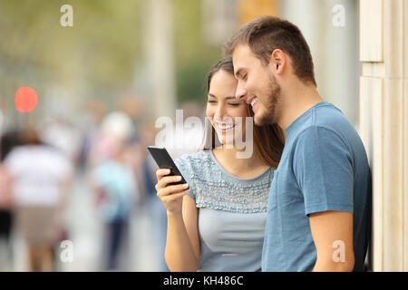 Couple watching on line media content in a smart phone standing on the street Stock Photo