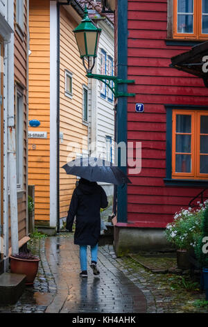 Unidentified person walking with a black umbrella through the narrow cobble stoned streets between colorful traditional houses in the old part of Berg Stock Photo
