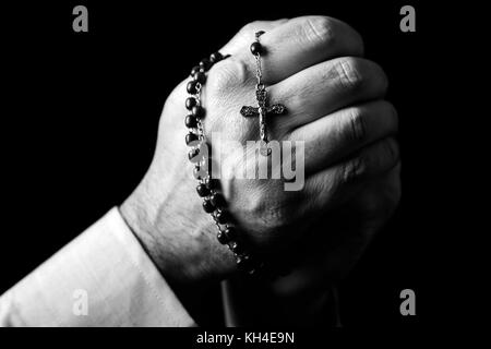 Male hands praying holding a rosary with Jesus Christ in the cross or Crucifix on black background. Mature man with Christian Catholic religious faith Stock Photo