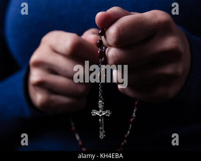 Female hands praying holding a rosary with Jesus Christ in the cross or Crucifix on black background. Woman with Christian Catholic hand faith Stock Photo