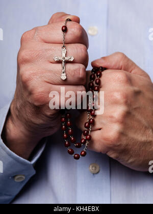 Male hands praying holding a rosary with Jesus Christ in the cross or Crucifix on black background. Mature man with Christian Catholic religious faith Stock Photo