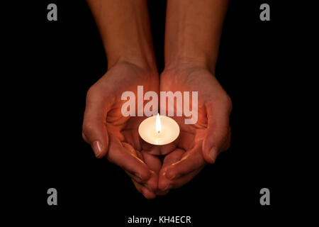 Hands holding and protecting lit or burning candle candlelight on darkness. Black background. Concept for prayer, praying, hope, vigil, night watch Stock Photo