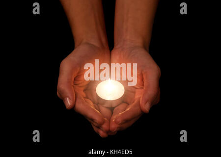 Hands holding and protecting lit or burning candle candlelight on darkness. Black background. Concept for prayer, praying, hope, vigil, night watch Stock Photo