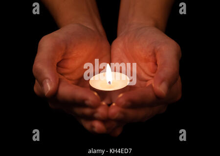 Hands holding and protecting lit or burning candle candlelight on darkness. Black background. Concept for prayer, praying, hope, vigil, night watch Stock Photo