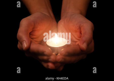 Hands holding and protecting lit or burning candle candlelight on darkness. Black background. Concept for prayer, praying, hope, vigil, night watch Stock Photo