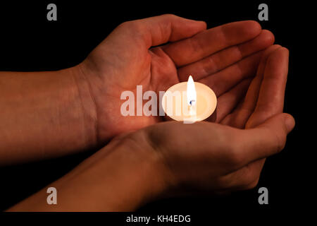 Hands holding and protecting lit or burning candle candlelight on darkness. Black background. Concept for prayer, praying, hope, vigil, night watch Stock Photo