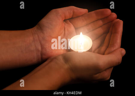 Hands holding and protecting lit or burning candle candlelight on darkness. Black background. Concept for prayer, praying, hope, vigil, night watch Stock Photo