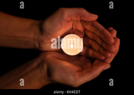 Hands holding and protecting lit or burning candle candlelight on darkness. Black background. Concept for prayer, praying, hope, vigil, night watch Stock Photo