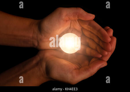 Hands holding and protecting lit or burning candle candlelight on darkness. Black background. Concept for prayer, praying, hope, vigil, night watch Stock Photo