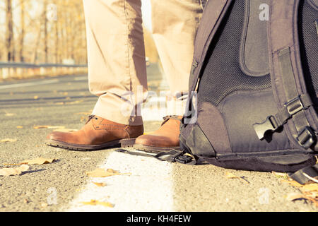 Feet and backpack of a male traveler or hitchhiker, wearing brown genuine autumn leather shoes as fall fashion concept Stock Photo