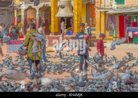 KATHMANDU, NEPAL OCTOBER 15, 2017: Unidentified people walking in the square surrounding of hundred of pigeons in front of a huge bell under a stoned gold structure in Kathmandu Boudhanath Stupa in Boudha town, Nepal Stock Photo