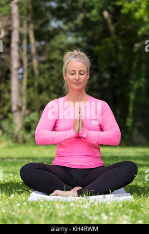 Mature middle aged fit healthy woman practicing yoga outside in a natural tranquil green environment Stock Photo
