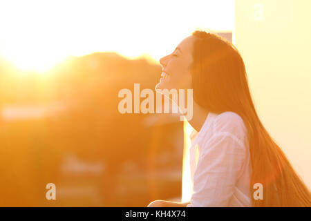 Side view portrait of a happy woman breathing deep fresh air at sunset in a house balcony Stock Photo