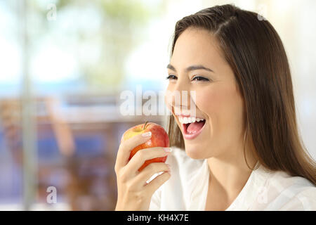 Portrait of a happy woman eating an apple in the living room at home Stock Photo