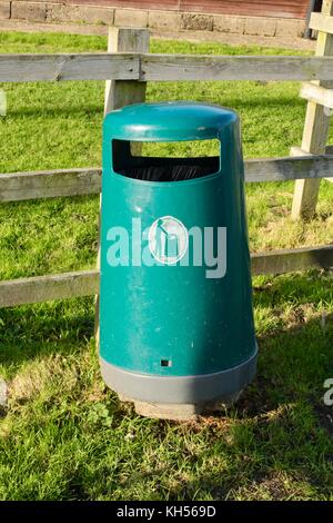 Green public litter bin from moulded plastic provided by council in England situated by a village playing field.coloured Stock Photo