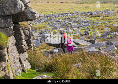 Couple walking with dog across granite outcrops at Great Mis Tor, Dartmoor National Park, Devon, UK in September Stock Photo