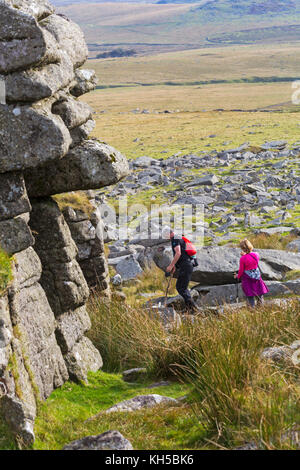 Couple walking with dog across granite outcrops at Great Mis Tor, Dartmoor National Park, Devon, UK in September Stock Photo