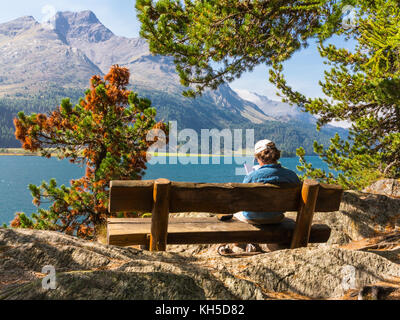 Reading a book sitting on the bench in front of the alpine lake in mountain Stock Photo