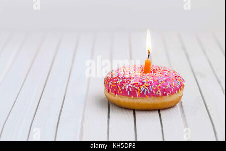 Birthday donut with pink glaze and colorful candies and burning candle , birthday concept Stock Photo