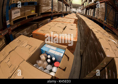 Pallets of USDA Emergency Food Assistance Program (TEFAP) commodities wait on the Houston Food Bank commodity warehouse shelves for movement to packing lines or delivery to food pantries; pallets in the aisles are loaded with disaster assistance packages (those with orange wrapping have USDA Foods in them), and are ready for delivery or distribution to those in need, in Houston, TX, on September 22, 2017. Houston Food Bank Operations Associate Director Marly Maskill provided the following information; in general, the food bank usually receives approximately 10 trucks per day and distributes ap Stock Photo