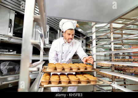 Baker man with a tray of cupcakes in his hands at work in Christ Stock Photo
