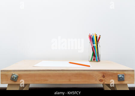 wooden child drawing table with color pencils by the white wall Stock Photo