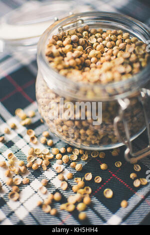 Gin and Whisky Ingredients: Coriander Seeds in glass jar on blue and white tartan Stock Photo