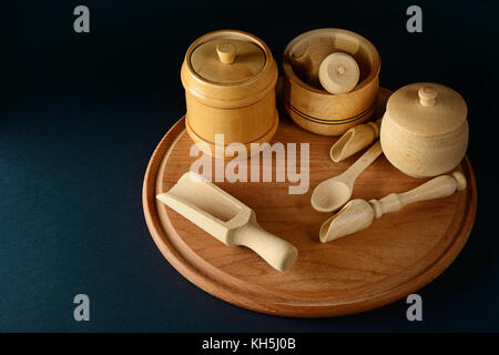 Wooden containers for products, spoon, cup, pestle, mortar on wooden board. Free space for text. Black background. Stock Photo