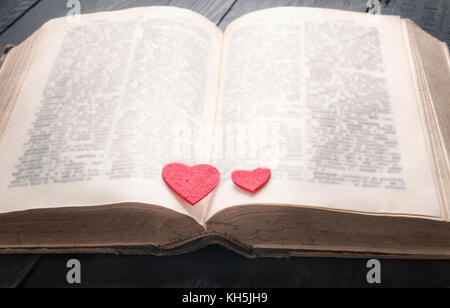 Two red hearts on the pages of an old open book, displayed on a vintage black table. A concept for the love of education,  a romantic novel or a love  Stock Photo
