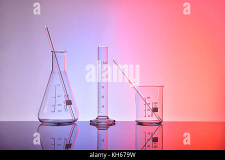 Supply of empty laboratory glass chemical containers on glass table isolated with red and blue lighting. Horizontal composition. Front view Stock Photo