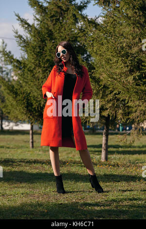 Outdoor portrait of a young beautiful fashionable woman, outdoors. The model, dressed in a stylish orange coat, sunglasses. The concept of women's fas Stock Photo