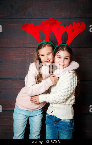 Two happy little smiling girls embracing .Christmas concept. Smiling funny sisters in deer horns in studio. Stock Photo