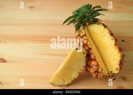 Piece of fresh ripe pineapple cut from the whole fruit isolated on wooden table Stock Photo