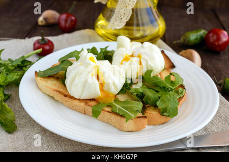 Boiled eggs in a pouch (poached) on crispy toast and green arugula leaves. Dietary breakfast. Stock Photo