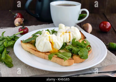 Boiled eggs in a pouch (poached) on toast and crisp green leaves of arugula and a cup of tea. Dietary breakfast. Stock Photo