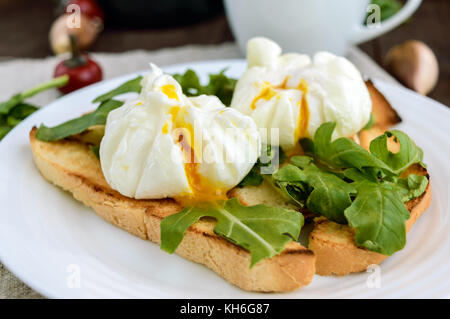 Boiled eggs in a pouch (poached) on crispy toast and green arugula leaves. Dietary breakfast. Close up Stock Photo