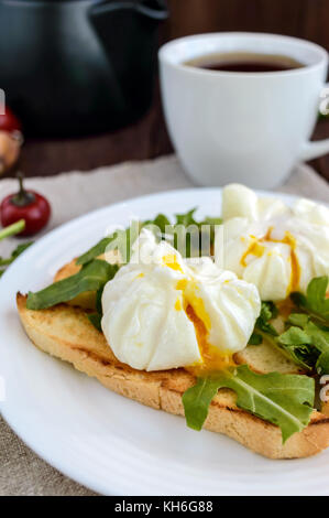 Boiled eggs in a pouch (poached) on toast and crisp green leaves of arugula and a cup of tea. Dietary breakfast. Stock Photo