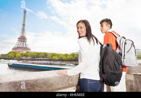 Young couple with backpacks standing at the embankment of Seine River and looking at the Eiffel Tower, Paris Stock Photo