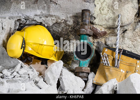 Demolition of walls. Electric hammer helmet and hearing protection lying on the rubble. Old brick and remodeled building wall. Grunt on the background Stock Photo