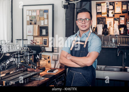 Male Barista cafe owner cross arms in store counter bar inside coffee shop, food and drink business start up. Stock Photo