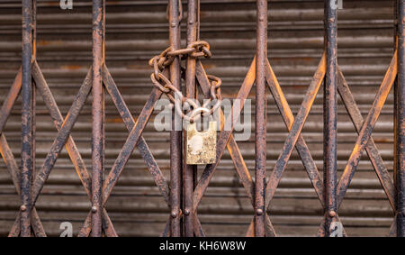 Closed collapsible gate with old rusty chain and lock in selective focus for background content. Stock Photo