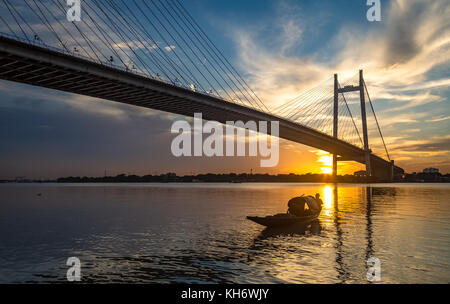 Cable bridge Vidyasagar Setu Kolkata on river Hooghly at sunset with wooden boats and moody sunset sky
