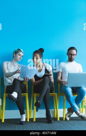 Executives discussing over document while using electronic gadgets in office Stock Photo