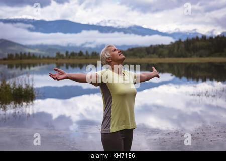Happy senior woman with arms outstretched standing near the lake Stock Photo
